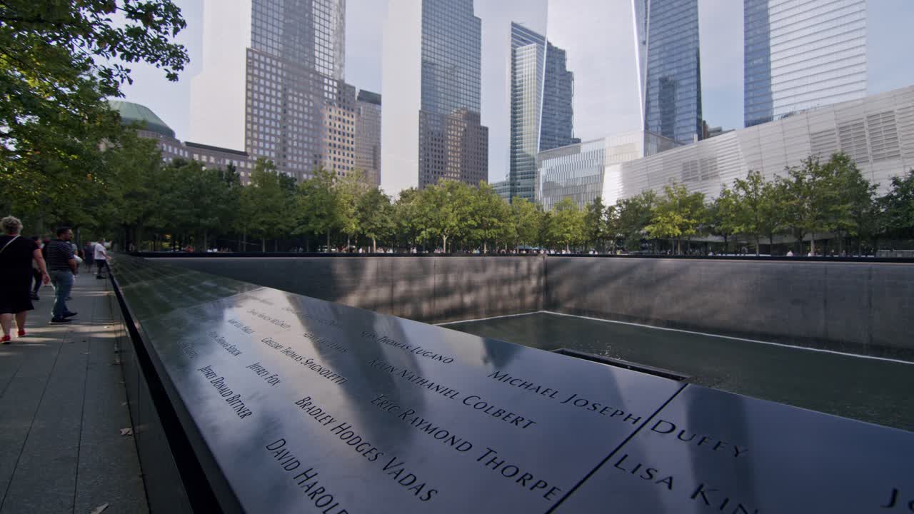 Visitors walk alongside the 9 11 Memorial in New York City, surrounded by skyscrapers and trees