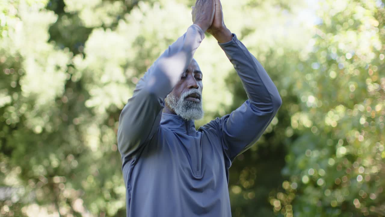 Uomo afroamericano porta i palmi delle mani dall'alto al petto, respirando e meditando, con una maglietta grigia all'aperto.