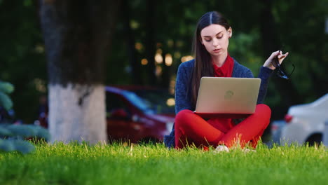 A-Young-Woman-Uses-A-Laptop-In-The-Park-In-The-Background-People-Walk-Hd-Video