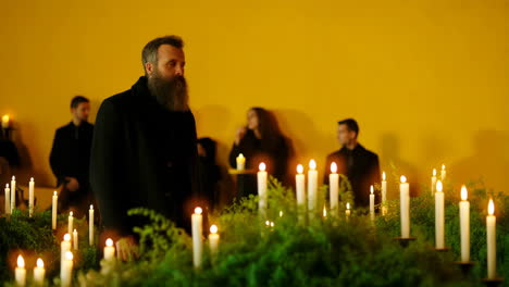 bearded man in black coat amidst candlelit ceremony