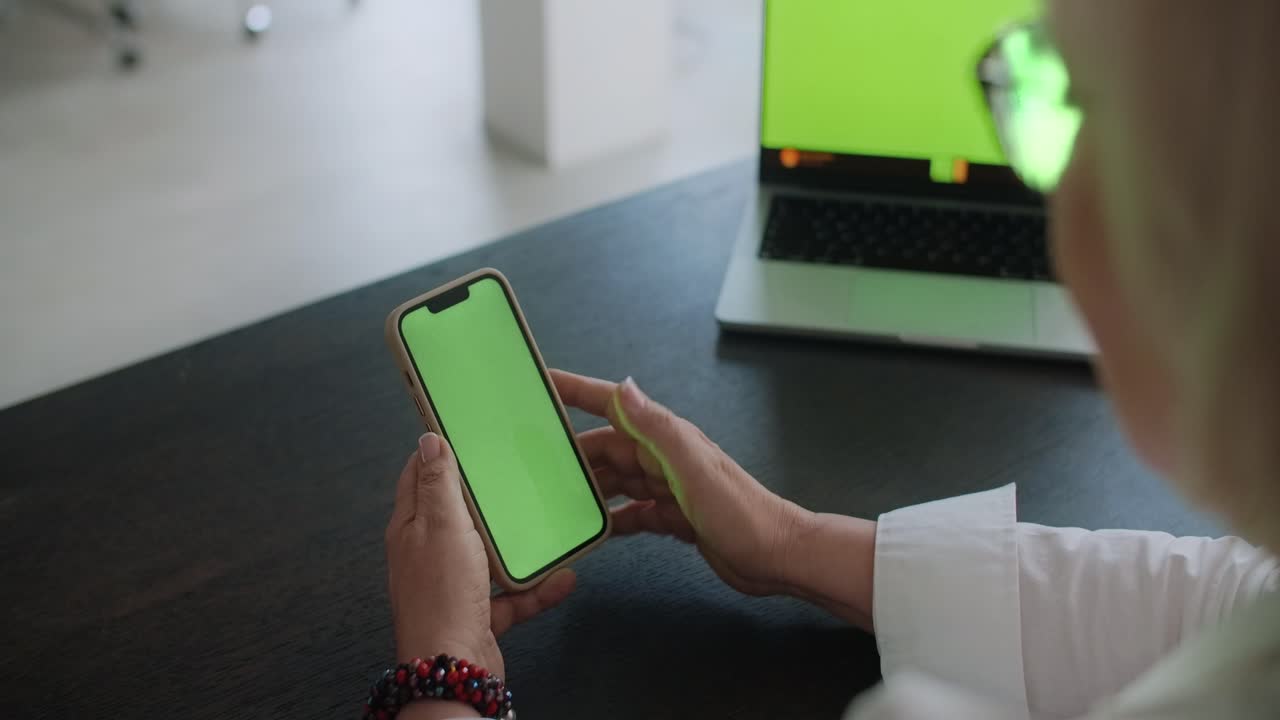 Woman using smartphone and laptop at a desk