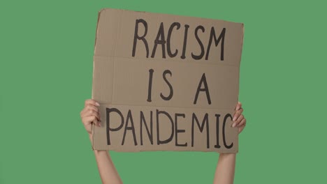 female hands hold a poster from a cardboard box with the words racism is a pandemic. protest against racism and police brutality. isolated a green screen, chroma key. close up. slow motion