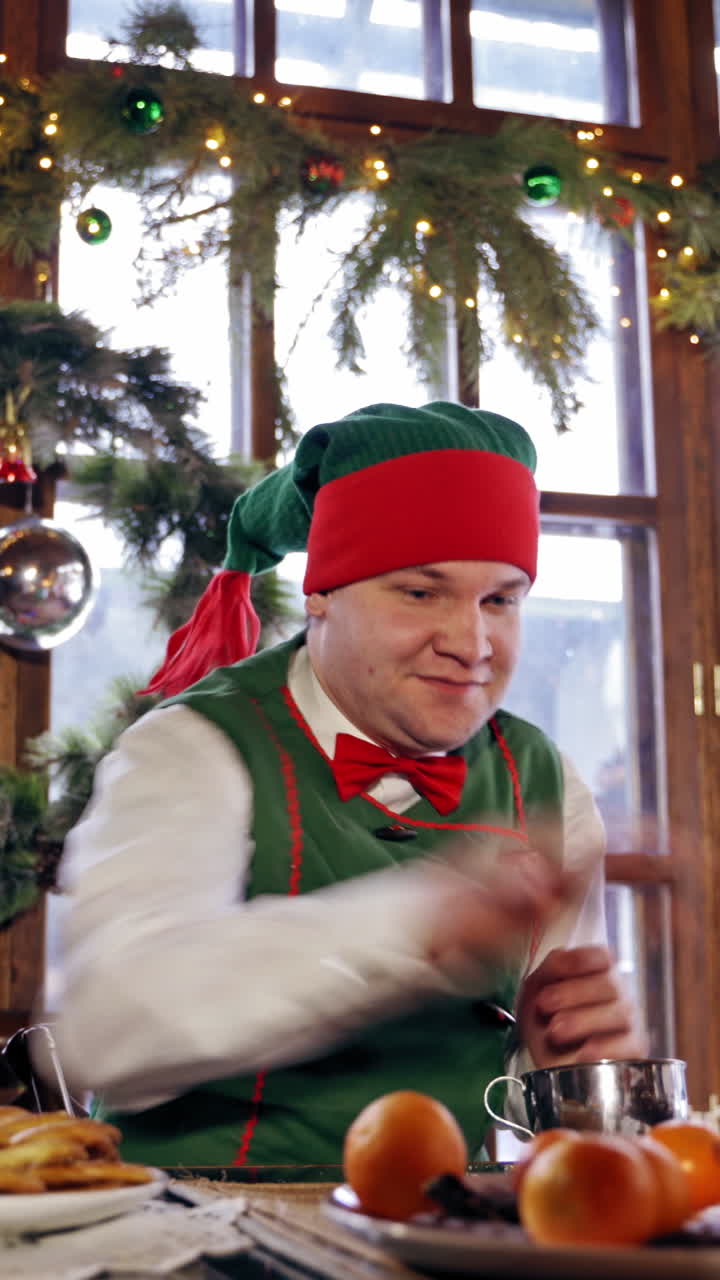 Elf playing tangerines at a table. Santas elf sitting at Christmas table in a decorated room. New Year celebration. Christmas eve. Vertical video