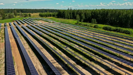 aerial rearview perspective of a large solar farm construction site with rows of panels in a green landscape, orbit along rows
