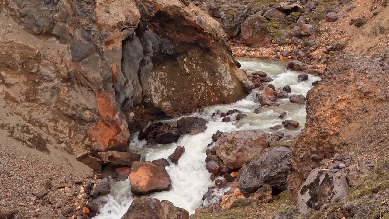vista cercana fija de un río de agua clara que fluye a través de un cañón, descendiendo de las montañas landmannalaugar en islandia