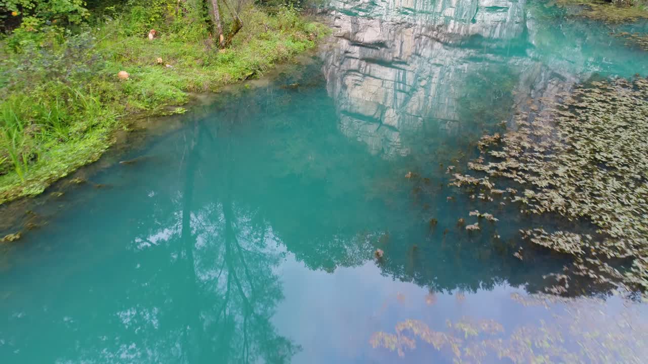 Slowly going over a blue river with lots of plants and grass. Beautiful reflection. Slovenija