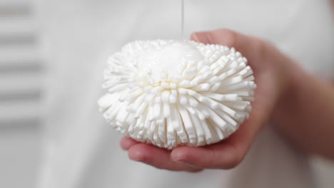 pouring shampoo on white sponge before shower, close up