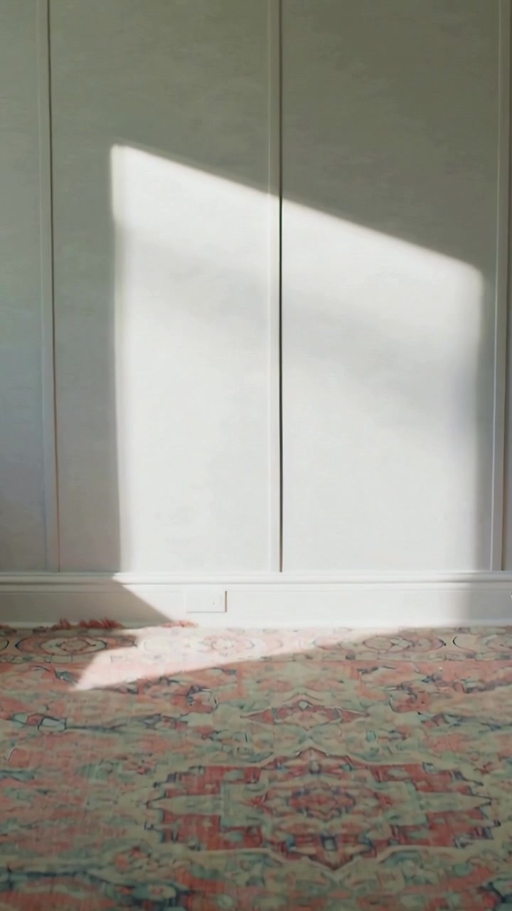 Vertical video: Sliding sunbeam down panel wall in room as sun shifting touching rug molding outlet