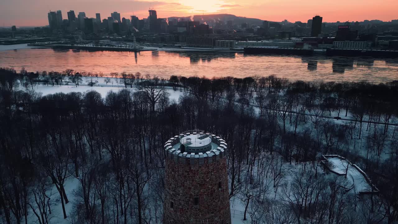 tomada aérea volando sobre la torre lewis en el parque jean drapeau y revelando el horizonte de la ciudad de montreal y el río saint laurent durante la temporada de invierno al atardecer, región de quebec, canadá