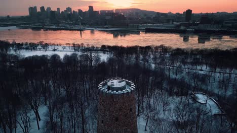 aerial shot flying over the levis tower in park jean drapeau and revealing montreal city skyline and saint laurent river during winter season at sunset, quebec region, canada