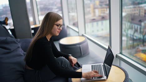 stylish young woman in office interior. beautiful business woman in glasses working on laptop computer near the window city view.