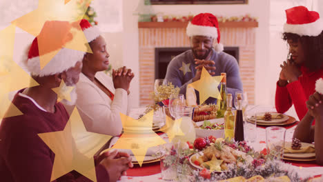 animation of stars falling over happy african american family wearing santa hats and praying