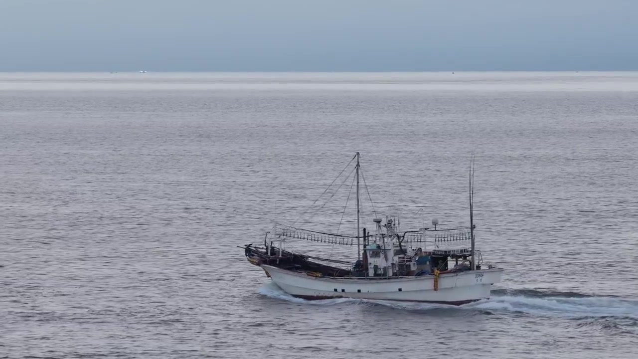 Inquadratura orizzontale in primo piano che segue una barca da pesca attraverso le acque vicino alla spiaggia di Gimnyeong, isola di Jeju, Corea del Sud.