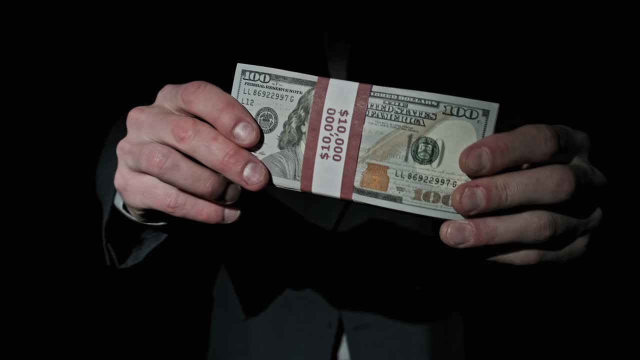 슈트를 입은 사업가는 검은 바탕에 1만 달러를 쌓아 놓은 모습을 보여준다.