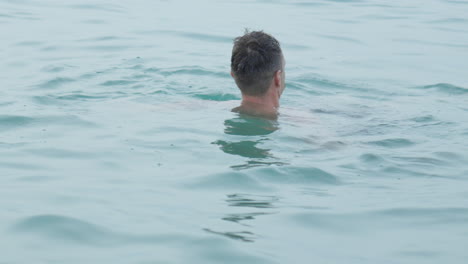 Close-Up-Shot-of-Man-Swimming-in-Calm-Sea-Water-on-a-Grey-Day