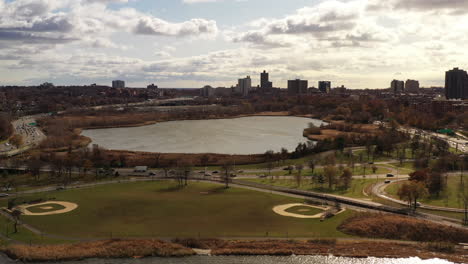 Plataforma-Rodante-Aérea-Sobre-Un-Lago-En-Un-Día-Nublado-Con-Campos-De-Béisbol-A-La-Vista