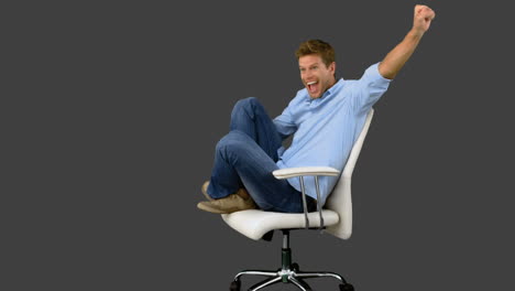 smiling man cheering and turning on swivel chair on grey screen