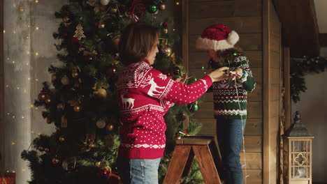 madre feliz e hija bailando y jugando juntas con luces mientras decoran el árbol de navidad en casa 1