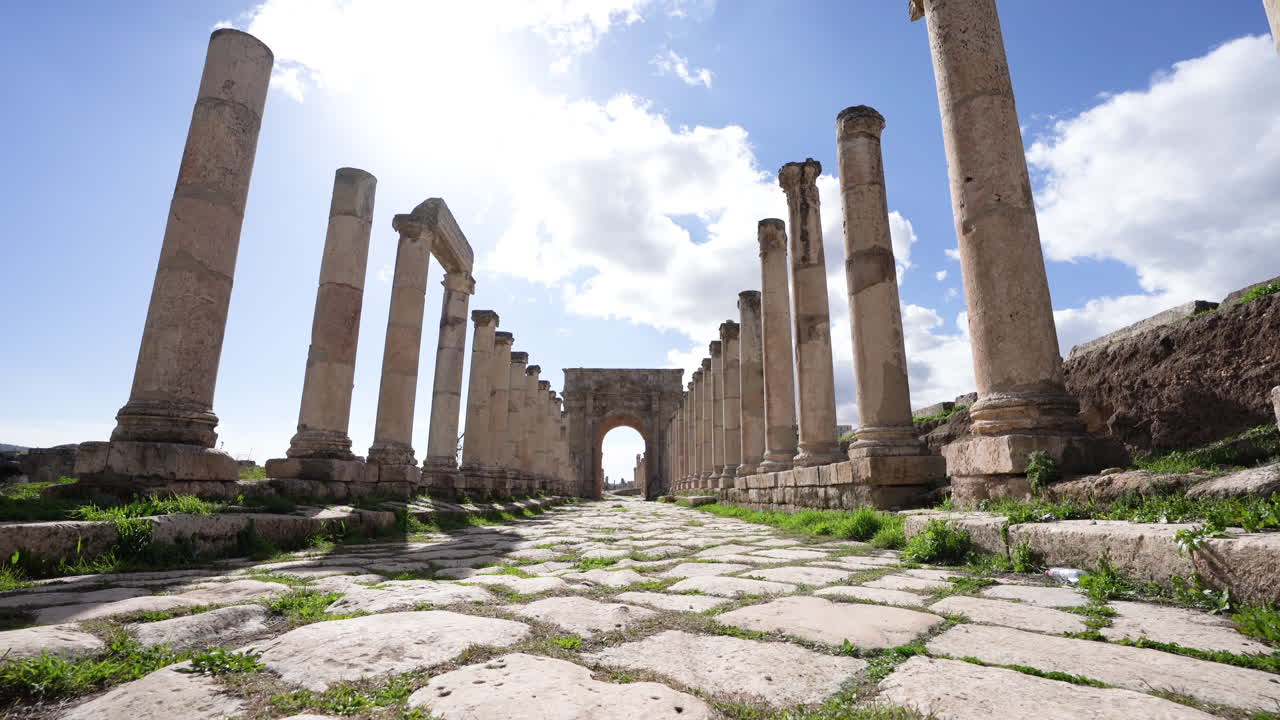ángulo bajo de altos pilares corintios y camino de piedra que conduce a un gran arco de piedra en ruinas romanas en jerash