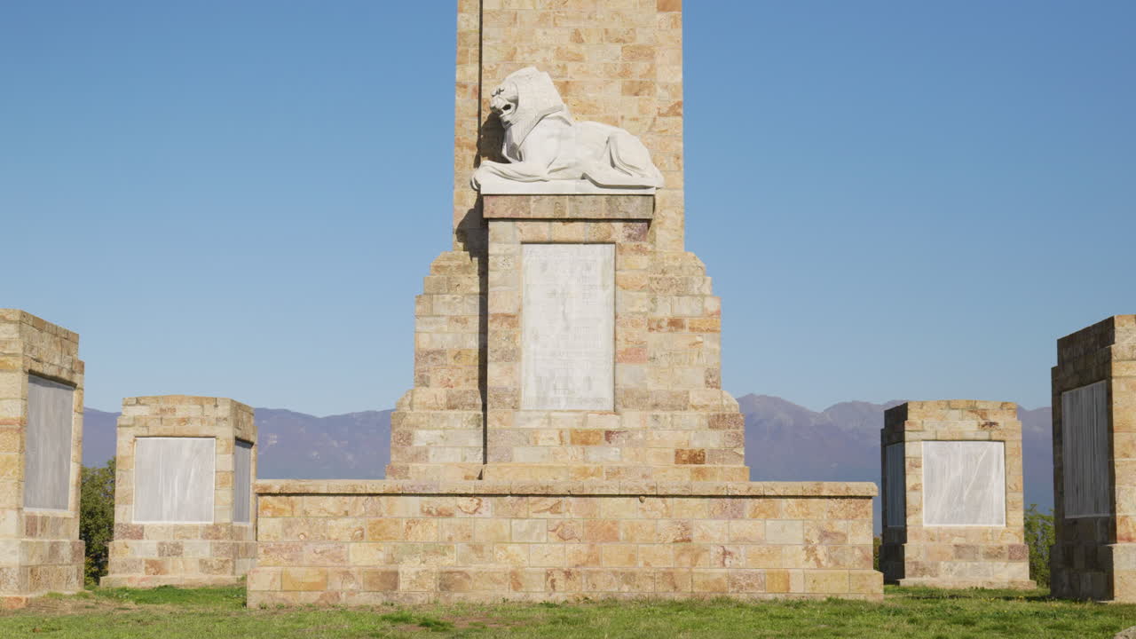 Vista grandangolare statica del Memoriale di Doiran nella Grecia settentrionale, con omaggio di corone, nomi di soldati incisi e statua di leone in marmo sotto cieli azzurri e sereni vicino al Lago Doiran.