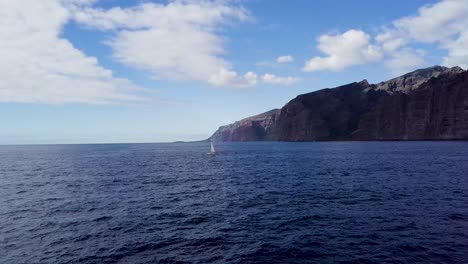 drone fly above blue ocean water with isolated sail boat in los gigantes tenerife canary island spain aerial footage