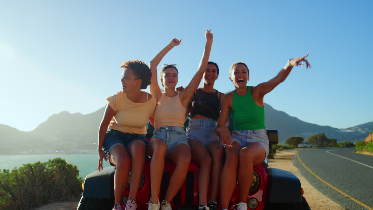 retrato de amigas riendo sentadas en el capó de un coche abierto en un viaje por carretera