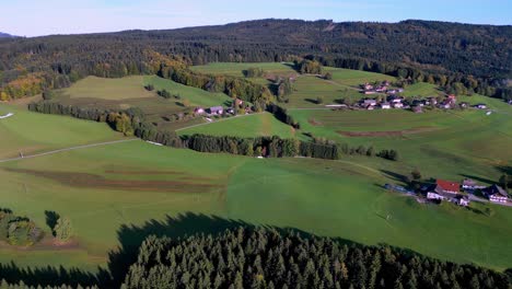 Aerial-view-of-a-small,-rural-village-nestled-amongst-green-fields-and-winding-roads,-with-a-backdrop-of-rolling-hills-and-distant-mountains