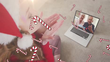 animación de bastones de caramelo cayendo sobre mujer caucásica en sombrero de santa en llamada de video portátil con la familia