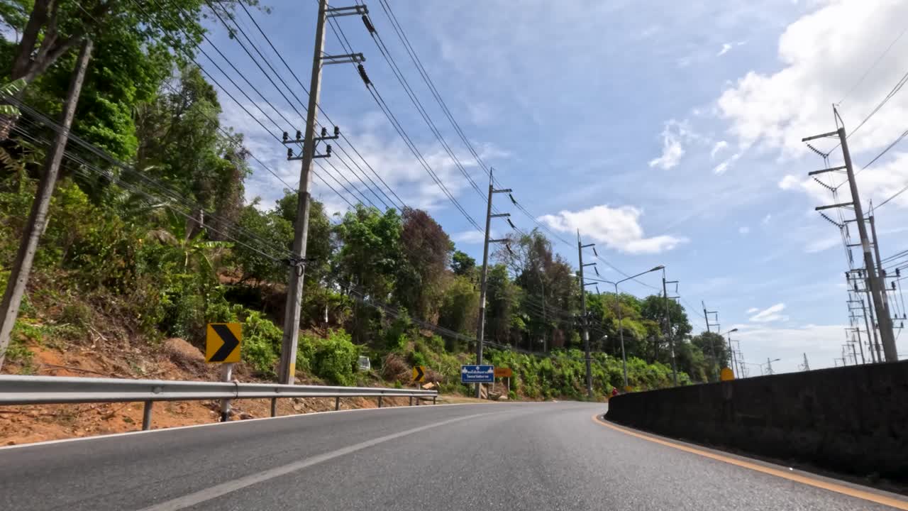 Low-angle timelapse of vehicles traveling a tropical mountain road in bright daylight, Phuket, Thailand