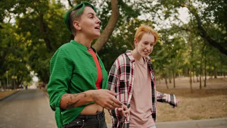 a lesbian girl with short green hair and a green shirt and her blonde girlfriend with short hair in a plaid shirt communicate and walk hand in hand and shrug their shoulders in the park during their date in the summer