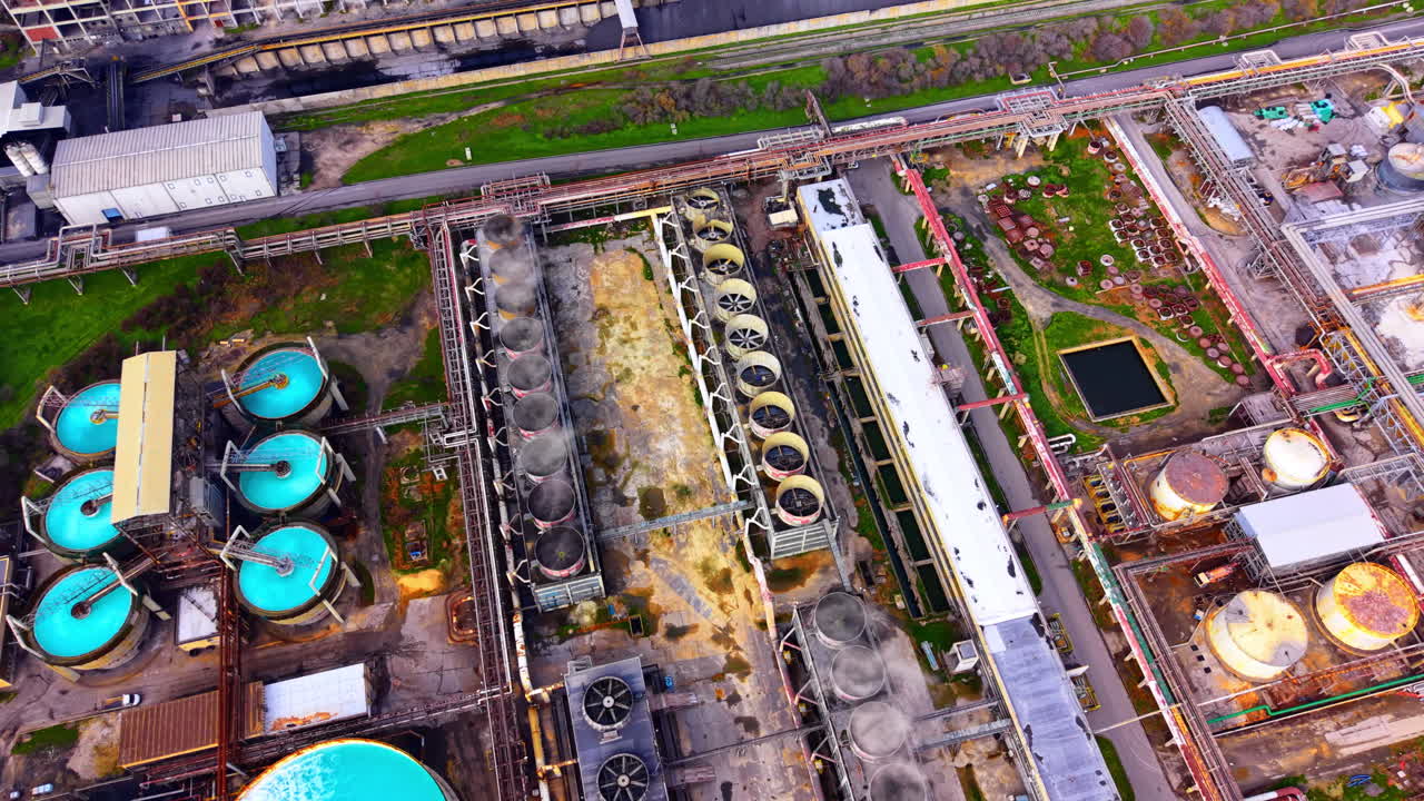 Circular blue liquid tanks and cooling towers inside an industrial complex with metal pipes and structures. Aerial view of industrial water treatment tanks