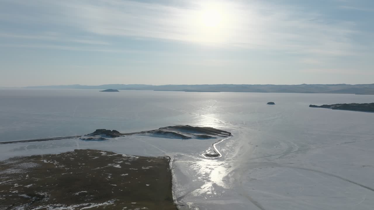 Riprese drone della superficie ghiacciata del Lago Baikal nello stretto di Maloye More, con piccole isole, chiazze di neve e riflessi del sole sul ghiaccio, Russia.