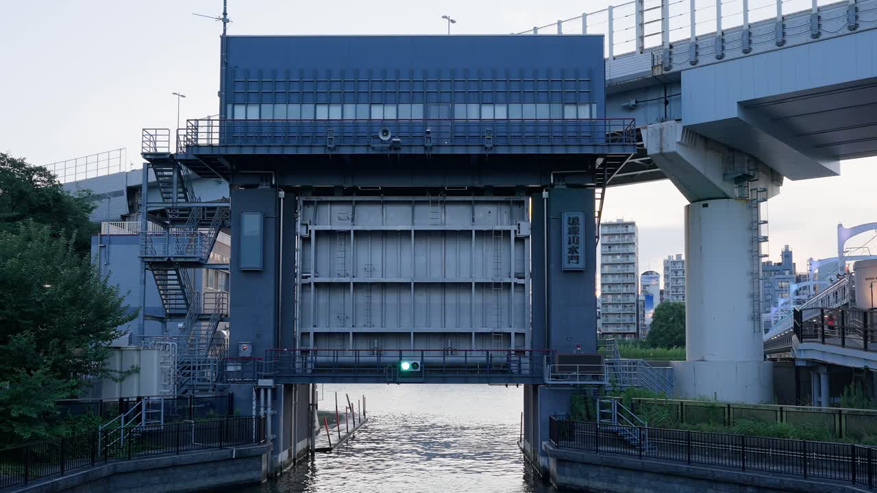 A shot of the Genmorikawa Sluice Gate located under the Shuto Expressway. The scene combines the sluice gate building with complex urban infrastructure