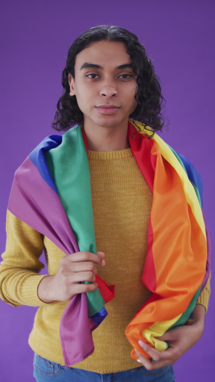 video vertical del retrato de un hombre biracial feliz sosteniendo una bandera lgbt