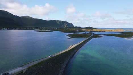 siguiendo el puente fredvang en lofoten, en el norte de noruega, con los coches circulando por él y el agua del mar que brilla en tonos azul turquesa claro y verde en un día soleado de verano