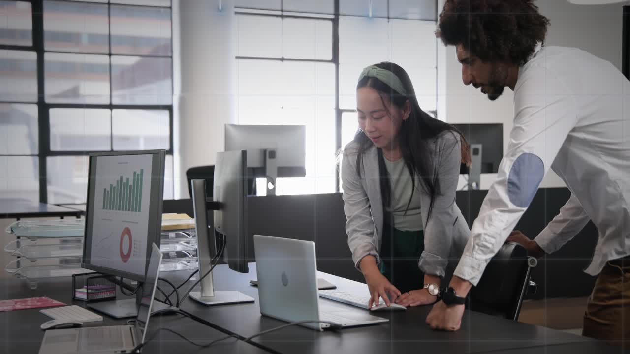 Dos compañeros de trabajo entrando en la oficina, acercándose al puesto de trabajo y analizando gráficos de negocio en el portátil