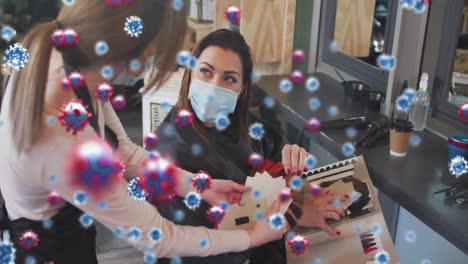 animation of coronavirus cells over caucasian female hairdresser and woman wearing face masks