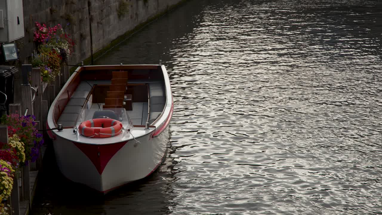 Stationary canal boat docked by flower-adorned pier, soft daylight, gentle water reflections, tranquil mood