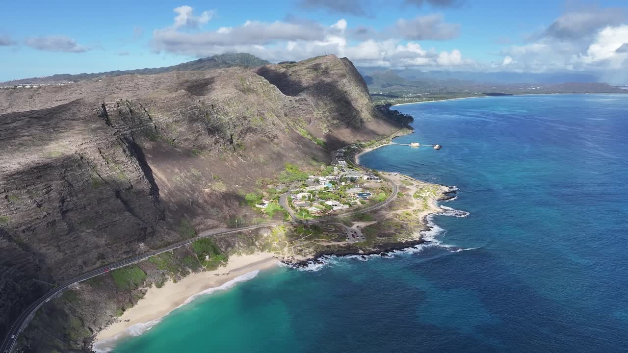 Aerial drone footage along Oahu’s windward coast, Hawaii's dramatic rocky cliffs, turquoise ocean waves crashing along the shoreline, lush tropical landscape., and the island’s rugged natural beauty
