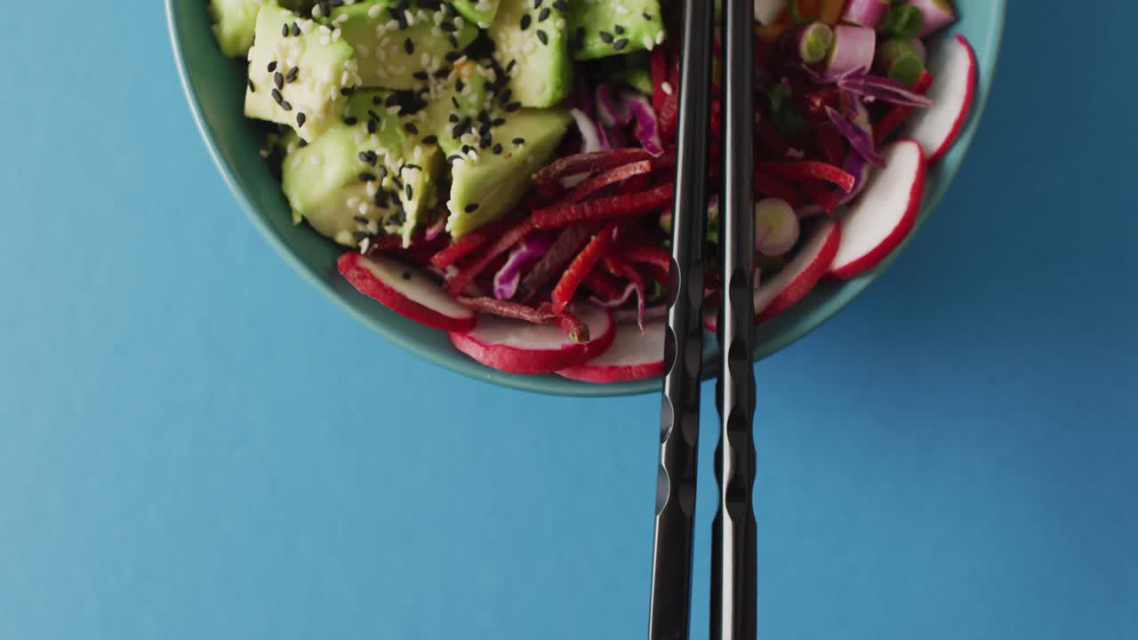 Composition of bowl of rice and vegetables with chopsticks on blue background