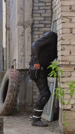 motorcyclist in leather moto suit and helmet runs fast into old abandoned building door taking part in quest game side view slow motion