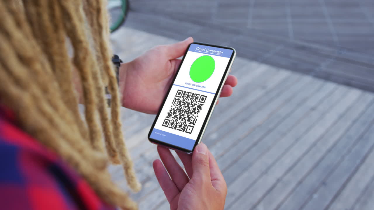 Man with dreadlocks holding smartphone with covid vaccination certificate and qr code on screen