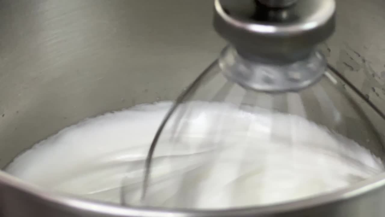 mezclador eléctrico comercial de trabajo pesado mezclando y azotando la clara de huevo hasta su pico, preparación para la crema de mantequilla suiza esponjosa, cámara lenta cinematográfica de primer plano