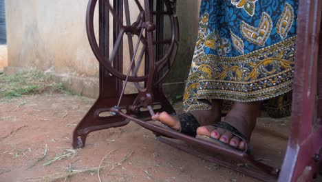 a close up shot of an african womens feet as she pedals a manual moving tailoring machine in africa