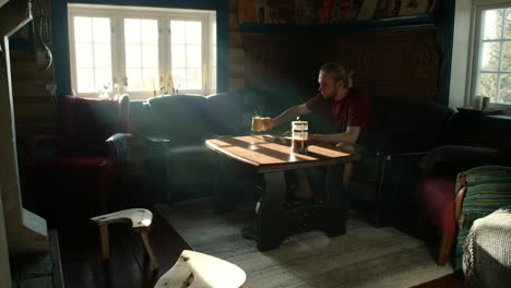 young man sitting in couch drinking coffee, thinking, designing and sketching product in traditional norwegian cabin in sunlight