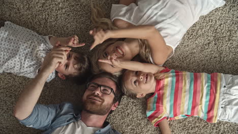 Top-View-Of-Father-And-Mother-And-Two-Children-Lying-On-The-Floor-With-Their-Heads-Together-And-Playing-With-The-Index-Finger