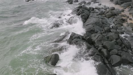 Slow-motion-aerial-footage-of-ocean-waves-crashing-up-against-rocks-in-Sierra-Leone,-Africa