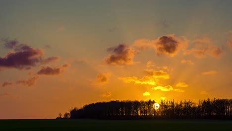 Lapso-De-Tiempo-De-Paisaje-Con-Bosque,-Puesta-De-Sol-Y-Cielo-Expresivo-Con-Nubes-Graduadas-Más-Azuladas-A-La-Deriva