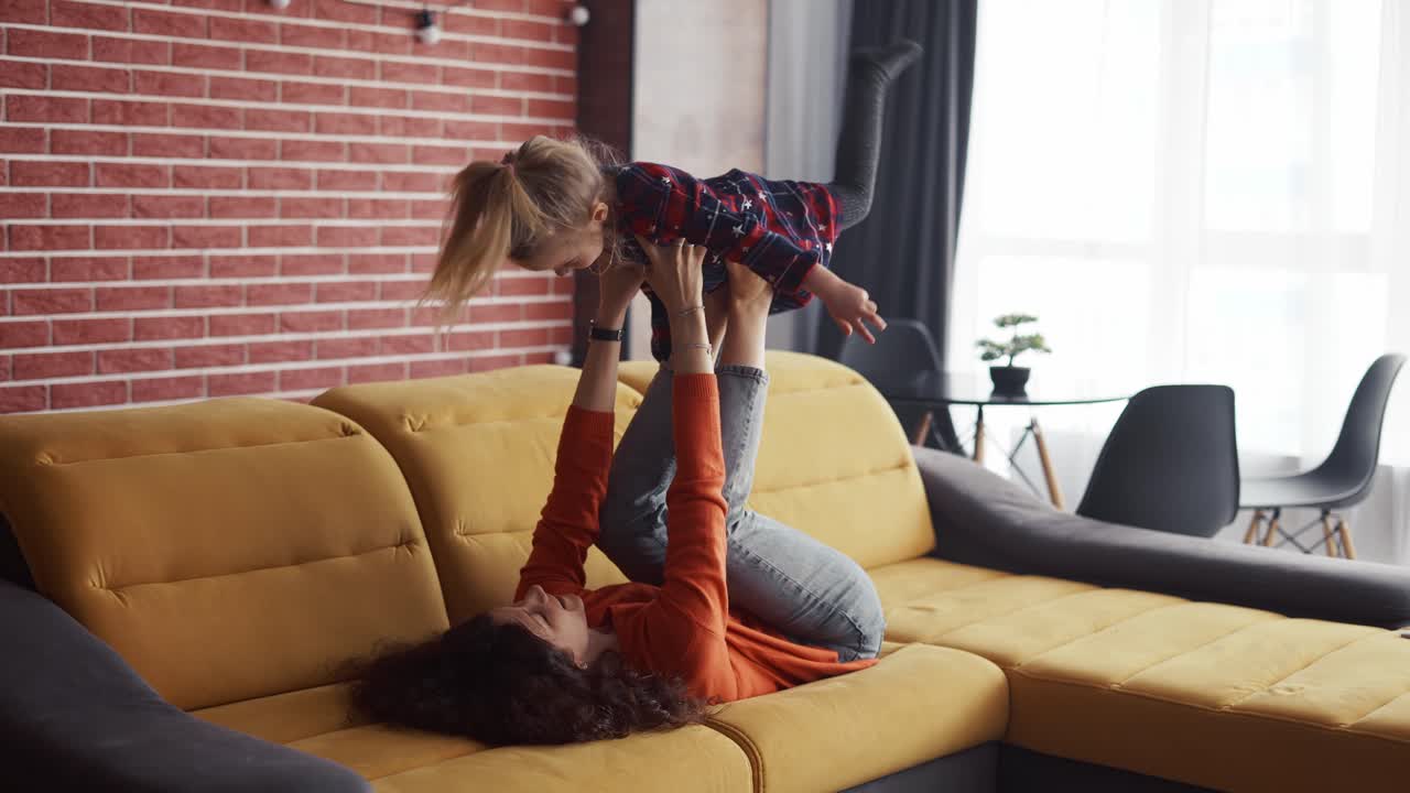 madre levantando a la niña en el aire en sus tobillos, fingiendo volar en casa