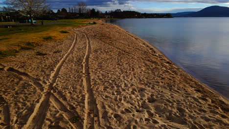 empty sand beach with tire tracks and gentle waves on shore in new zealand